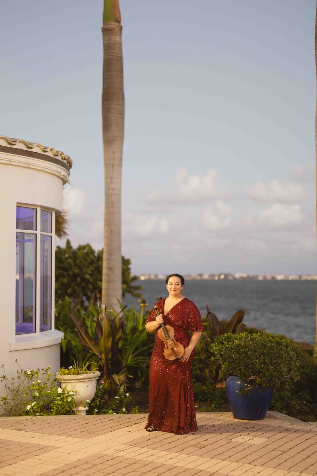 Founder of Luxe Harmony in a red gown holding her violin, offering information about wedding violinist prices.
