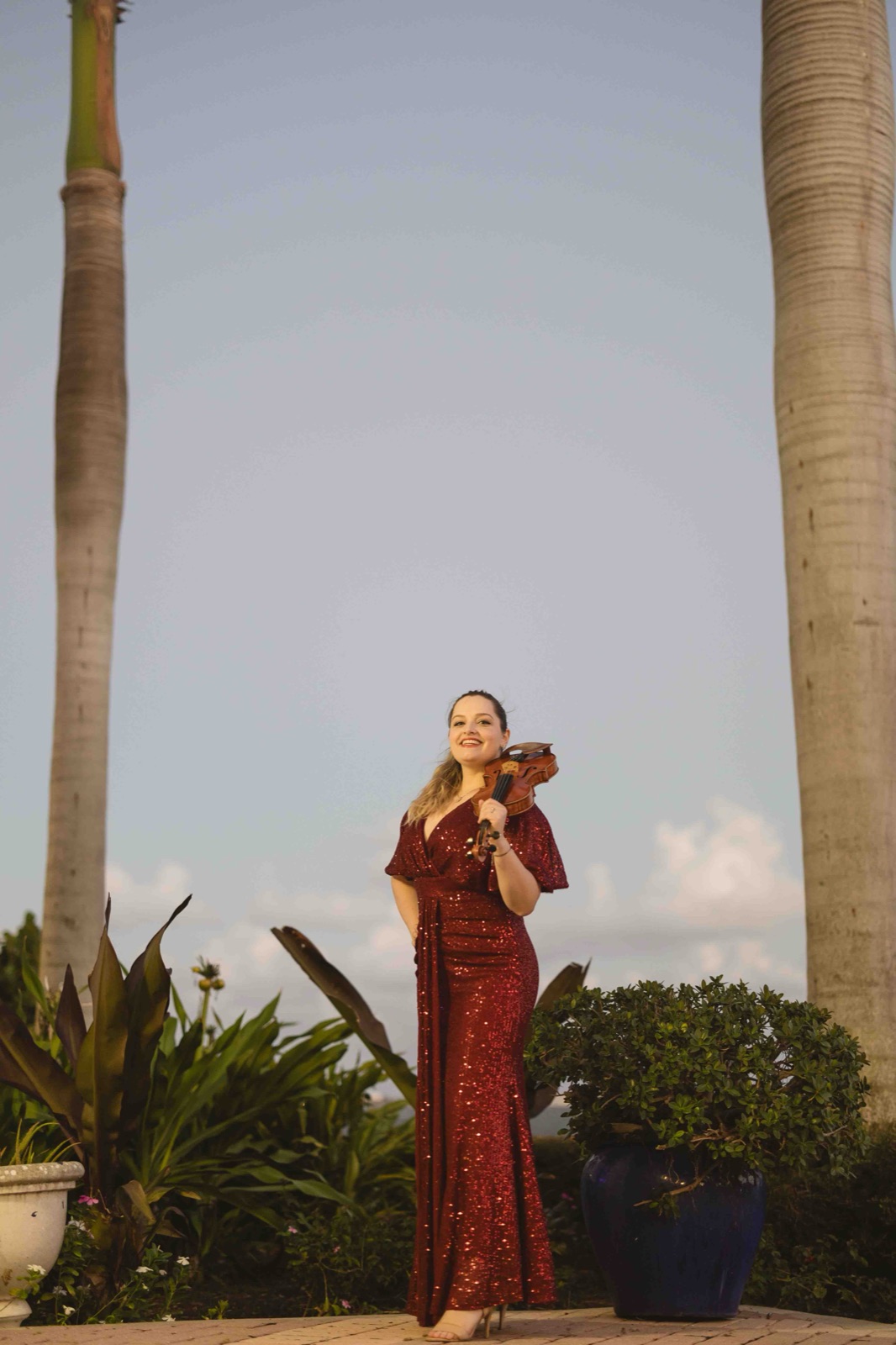 Wedding violinist in a red gown holding her violin, offering elegant music options and information about wedding violinist prices.